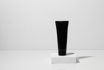 Simple aestaestheti cosmetic baclground with black tube on the podium with shadow