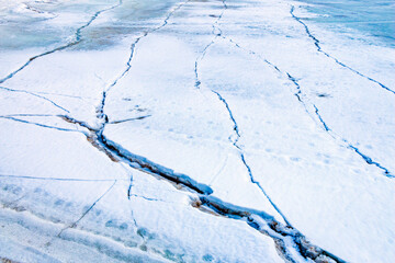 Cracks on thick ice on surface of  frozen river in winter season, powdered by snow and sand, with brilliant snow and ice crystals.