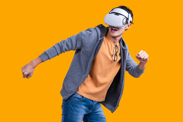 excited asian adult male wearing headset vr virtual goggle gadget in sport casual cloth playing sport online game with fun and joyful facial expression on yellow background studio shot