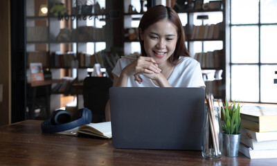 Smiling asian undergraduate teen girl student study in library with laptop books doing online research for coursework, making notes for essay homework assignment, online education e-learning concept