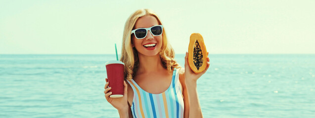 Summer portrait of happy smiling young woman with papaya and cup of juice on the beach on sea...
