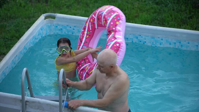 Little girl and happy grandfather having fun together in outdoors swimming pool, granddaughter.