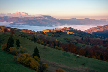 mountainous rural landscape at sunrise. fields and pastures on rolling hill in morning light. cloud...