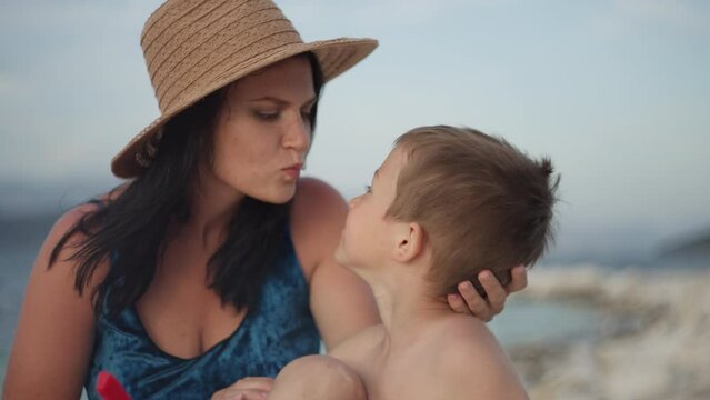 Mom and son playing on the beach by the sea. Happy childhood smiling baby and dink by the ocean together.