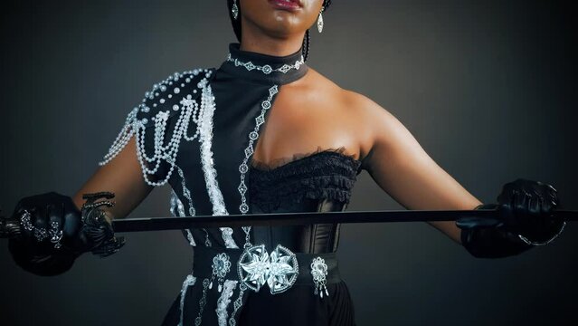 closeup portrait african fantasy woman warrior queen holding sword in hands sharp blade back rear view, sexy face girl princess fashion model posing. black dress creative design, dark gray studio.