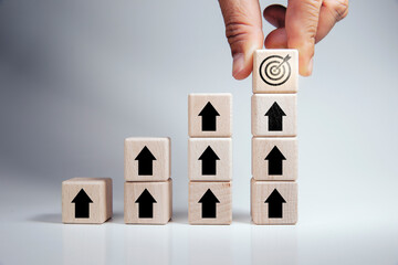 business growth concept of success of business goals Wooden cube with "target" icon on top of stacked wooden cubes standing with rising arrow icons on white background goals, vision, plans, actions