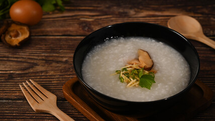 Congee or Rice porridge with boiled egg ,sliced ginger and slice scallion in bowl on wooden table for breakfast or light meal