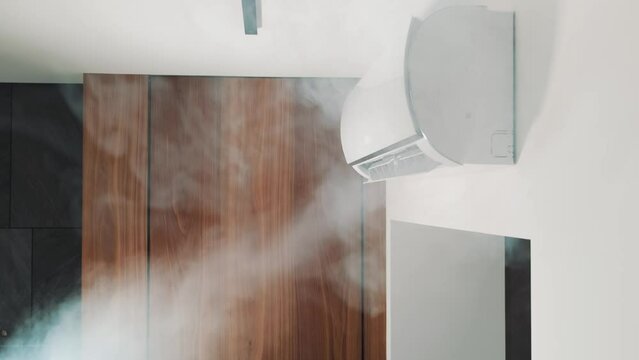 Close-up shot indoor unit air conditioning in room attached on wall. Flow of cold, frosty air, cooling house. Modern technologies. Turns on wing goes down, blinds are opened, drives cold air. Video 4k
