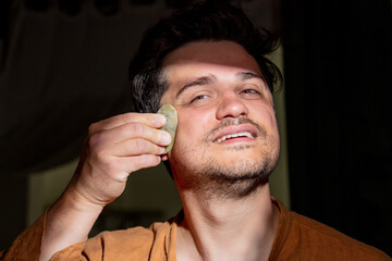 Obraz premium 30 year old man massaging his face with a stone in bathroom