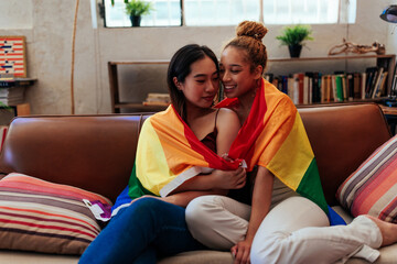 Lesbian couple hugging with rainbow flag at home