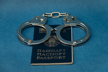 Belarusian passport and handcuffs on a blue background. The concept of illegal detentions and arrests, trials of demonstrators, political repressions against the opposition.