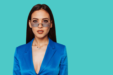 Fashion arabic girl with long hair and transparent sunglasses in a blue suit poses over blue background in the studio.