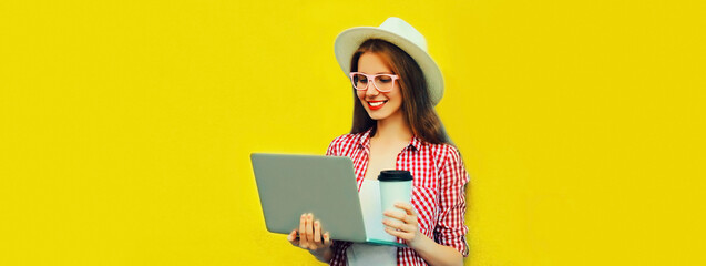 Portrait of modern young woman working with laptop drinking coffee on yellow background