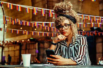 Portrait of serious woman with afro hairstyle reading news on smartphone sitting in a coffeehouse shot