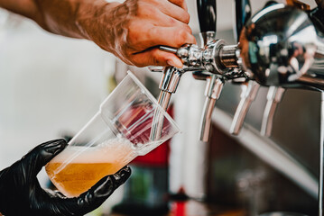hand at beer tap pouring a draught beer in plastic glass serving in a cafe
