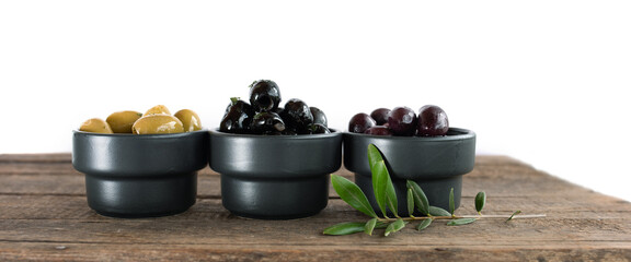 Different varieties of olives on rustic wooden table with olive branch isolated on white...