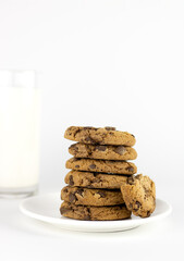 Plate with chocolate chip cookies and glass of milk on white background