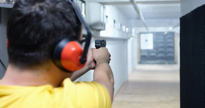 Rear view of man aiming gun at target in shooting range