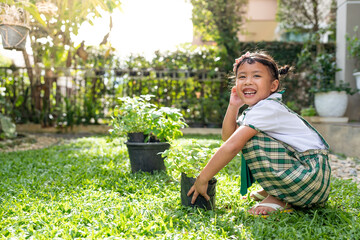 Adorable Schoolgirl holding home plant in black bag at garden.