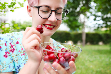 woman in blue dress holding handful of sweet cherries in garden farm orchard on summer day.