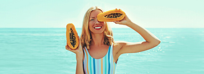 Summer portrait of happy smiling young woman with papaya on the beach on sea background