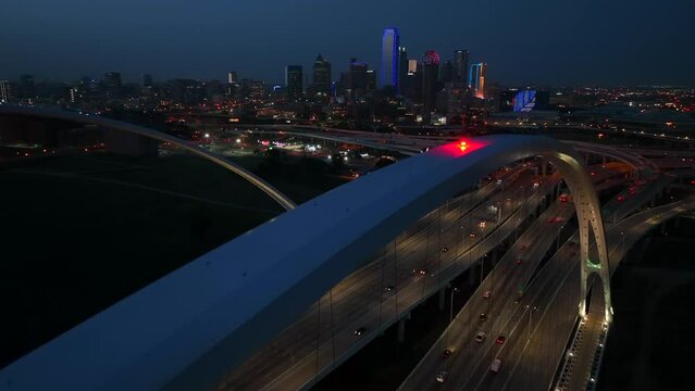 Downtown Dallas TX aerial establishing shot of skyline at night. Margaret McDermott Bridge in evening view in dark. Traffic on I-30.