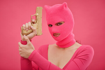 Portrait of gangster girl in pink holding gun and protecting herself isolated on pink background - obrazy, fototapety, plakaty