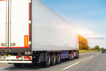 Obraz na płótnie Canvas White blank modern delivery big shipment cargo commercial semi trailer truck moving fast on motorway road city urban suburb. Business distribution logistics service. Lorry driving highway sunny day