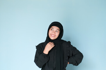 Naklejka na ściany i meble Happy expression of beautiful Asian girl in hijab in black shirt on light blue background
