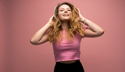 Fototapeta na wymiar Young woman listening music in headphones and dancing with a smile face and stand over pink background. Attractive lady enjoying song copy space.