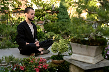 young handsome man meditating in the bonsai garden