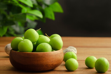 green plum in wooden bamboo bowl and black background