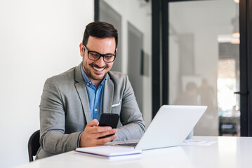 Fototapeta premium Happy entrepreneur networking on mobile phone while sitting at office desk
