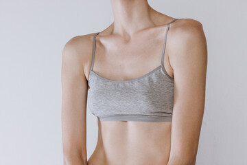 Cropped image of female breast in cotton underwear isolated over grey studio background. Plastic surgery. Mammoplasty