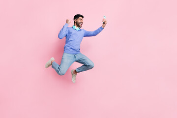Full length photo of funny lucky arabian man wear long sleeve shirt blogging gadget jumping running...