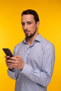 A Guy In A Blue Shirt Holds A Mobile Phone In His Hands And Looks With A Smirk