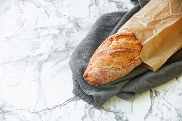 Rustic sourdough baguette on kitchen towel on marble table. Free space for text
