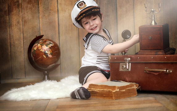 A child in a retro interior and an old phone sits on the floor. A small child is a traveler in vintage decorations. Child traveler is calling phone.