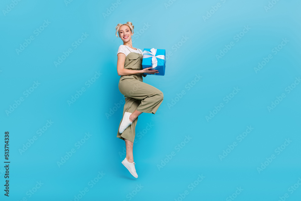 Sticker Full body photo of sweet young blond lady jump with present wear t-shirt overall shoes isolated on blue background