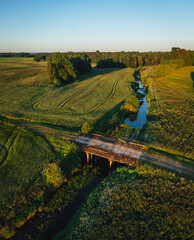 Aerial view on small countryside river in sunset time with old bridge, latvian country side view