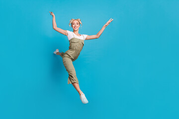 Fototapeta premium Full length photo of funky young lady jump wear t-shirt grey overall sneakers isolated on blue background
