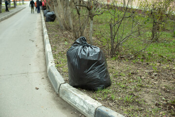 Bag is black. Garbage bag on road. Cleaning of territory.