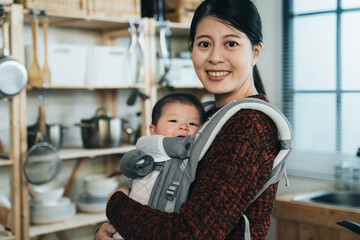 profile happy beautiful asian mother is smiling at camera while carrying her lovely new baby in a...