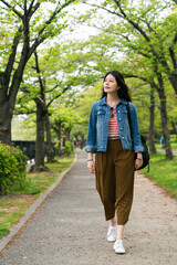 full length with vertical shot of beautiful asian female surrounded with trees enjoying breeze and nature while walking in the park in Osaka, japan.