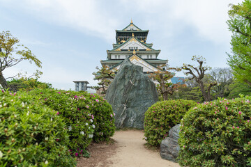 beautiful Osaka castle at distance against sunny blue sky and blocked by a rock at the end of bush garden path in japan
