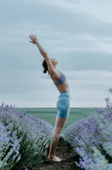 Woman in pastel tones activewear doing yoga pose backbend in the middle of a lavender field on a cloudy day.