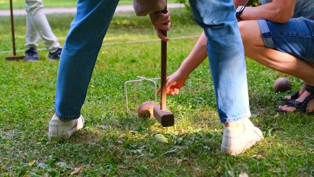 Person plays a sports game of croquet on a green field strike mallets on a ball and conducts through hoops. 