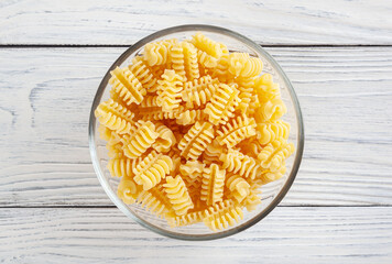 Uncooked radiatori pasta in glass bowl on white wooden background