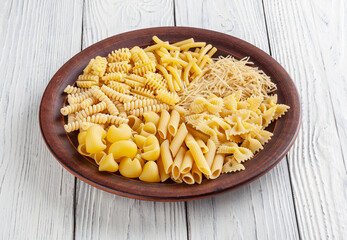 Different types and shapes of Italian pasta in ceramic plate on white wooden background