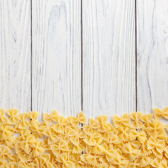 Uncooked farfalle rigate pasta on white wooden background with copy space